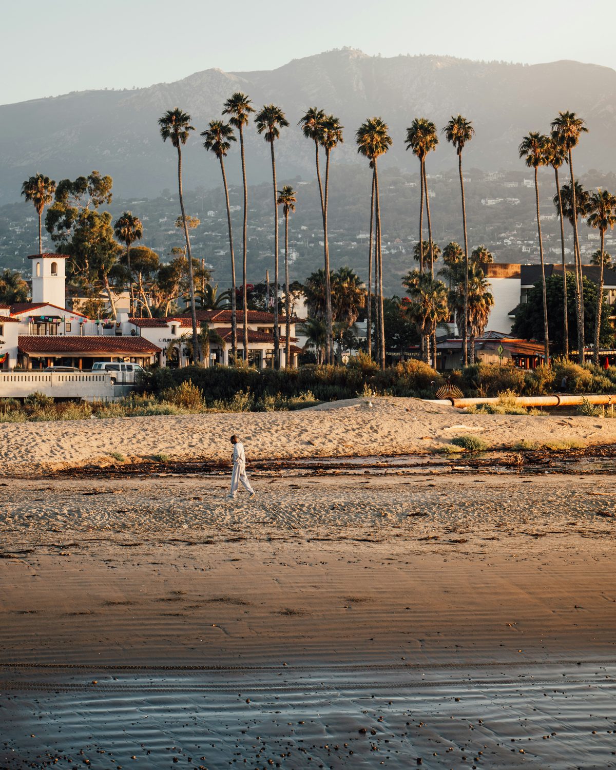 Tall palms and Spanish-style rooftops below the Santa Ynez Mountains at golden hour